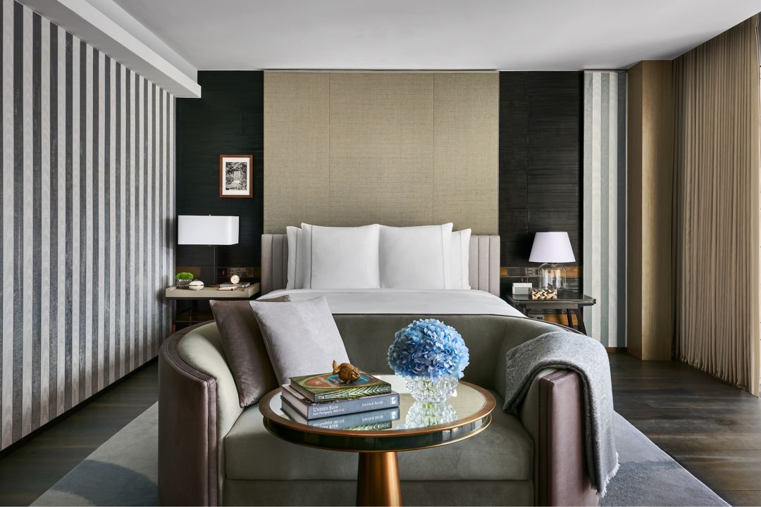 A luxurious hotel bedroom with a large bed, two nightstands, and a sofa with a coffee table.